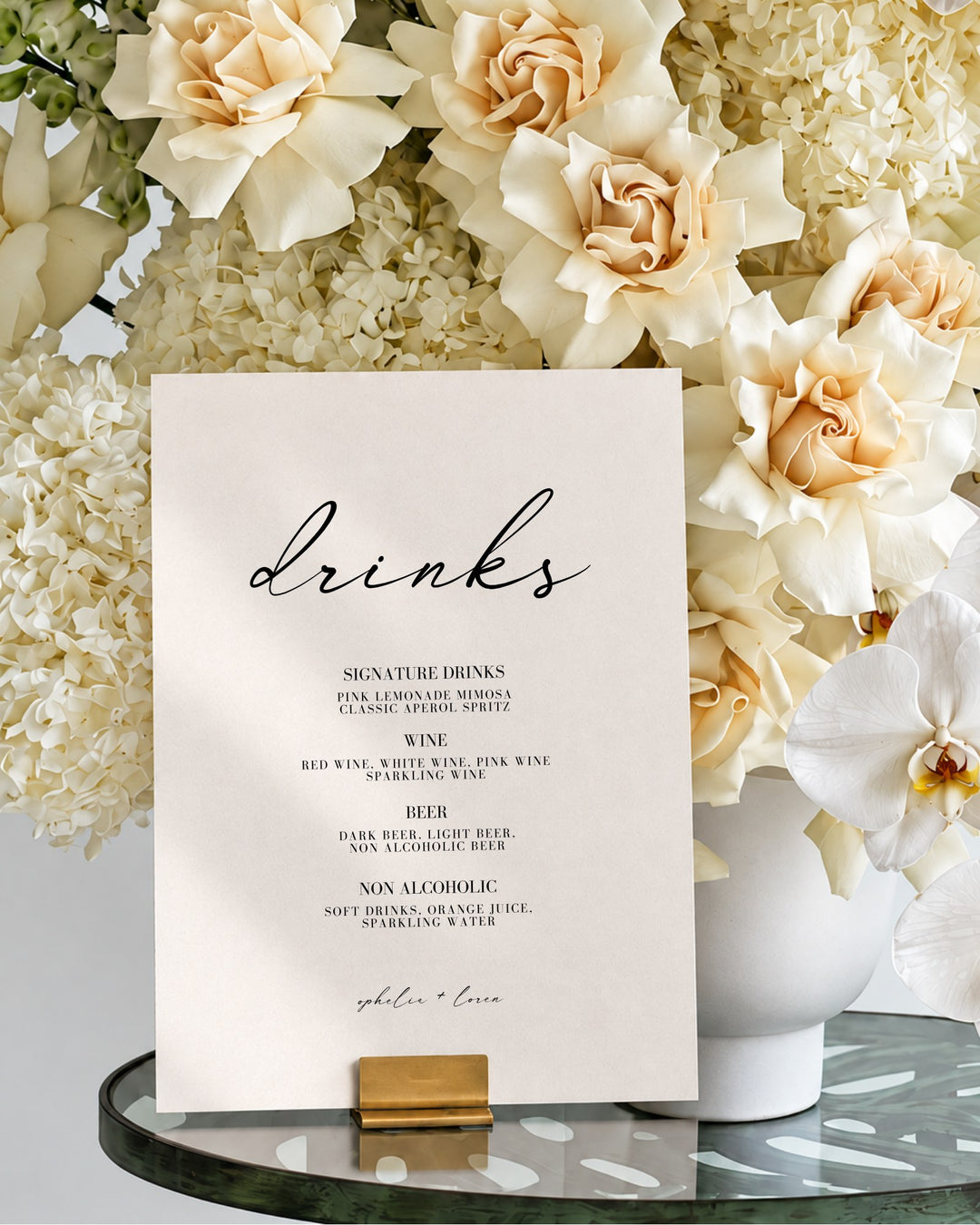 Aria acrylic wedding bar and drinks sign in a gold holder on a glass table in front of ivory roses and hydrangeas