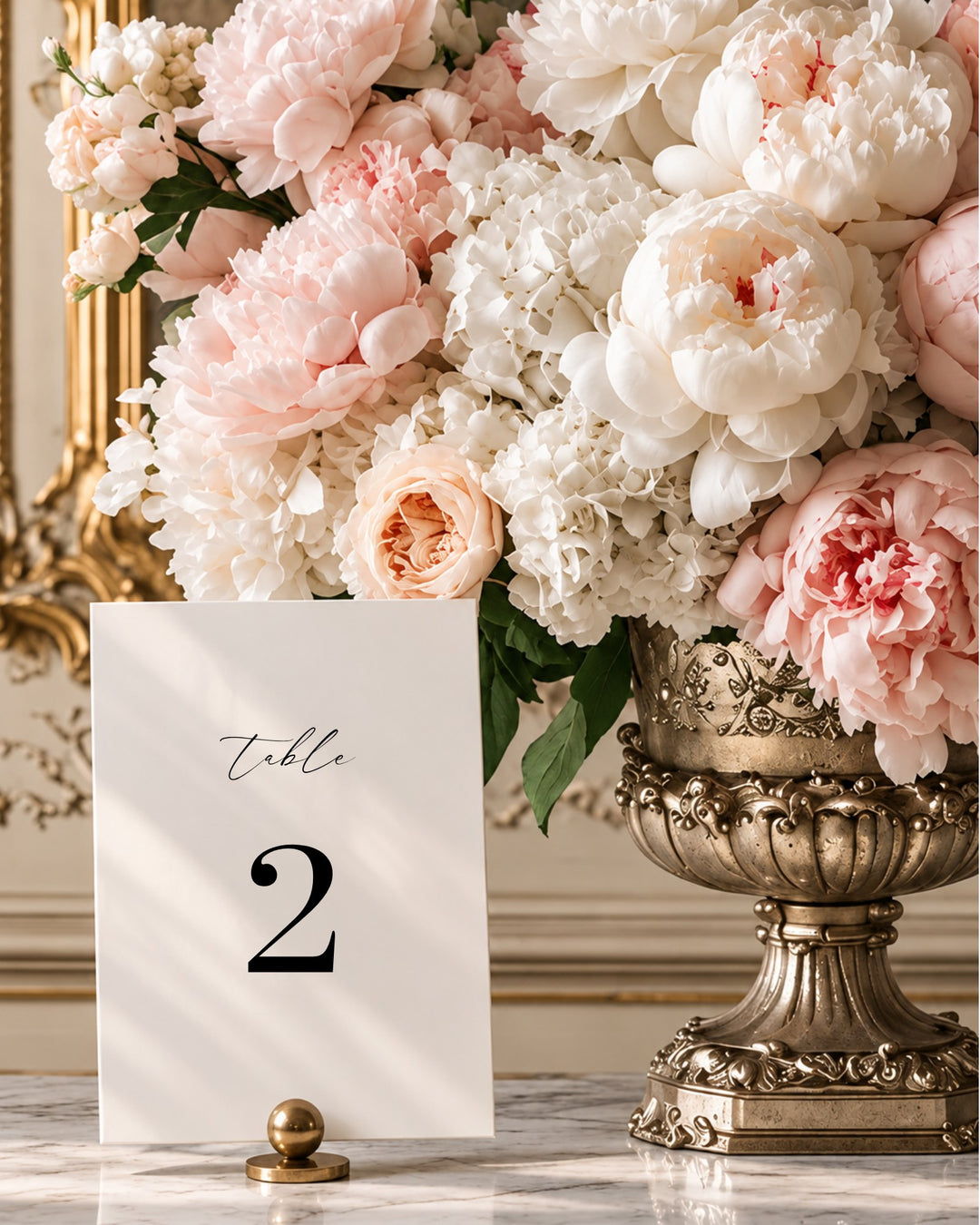 Aria acrylic wedding table number in a gold holder beside blush peonies in a gilded urn