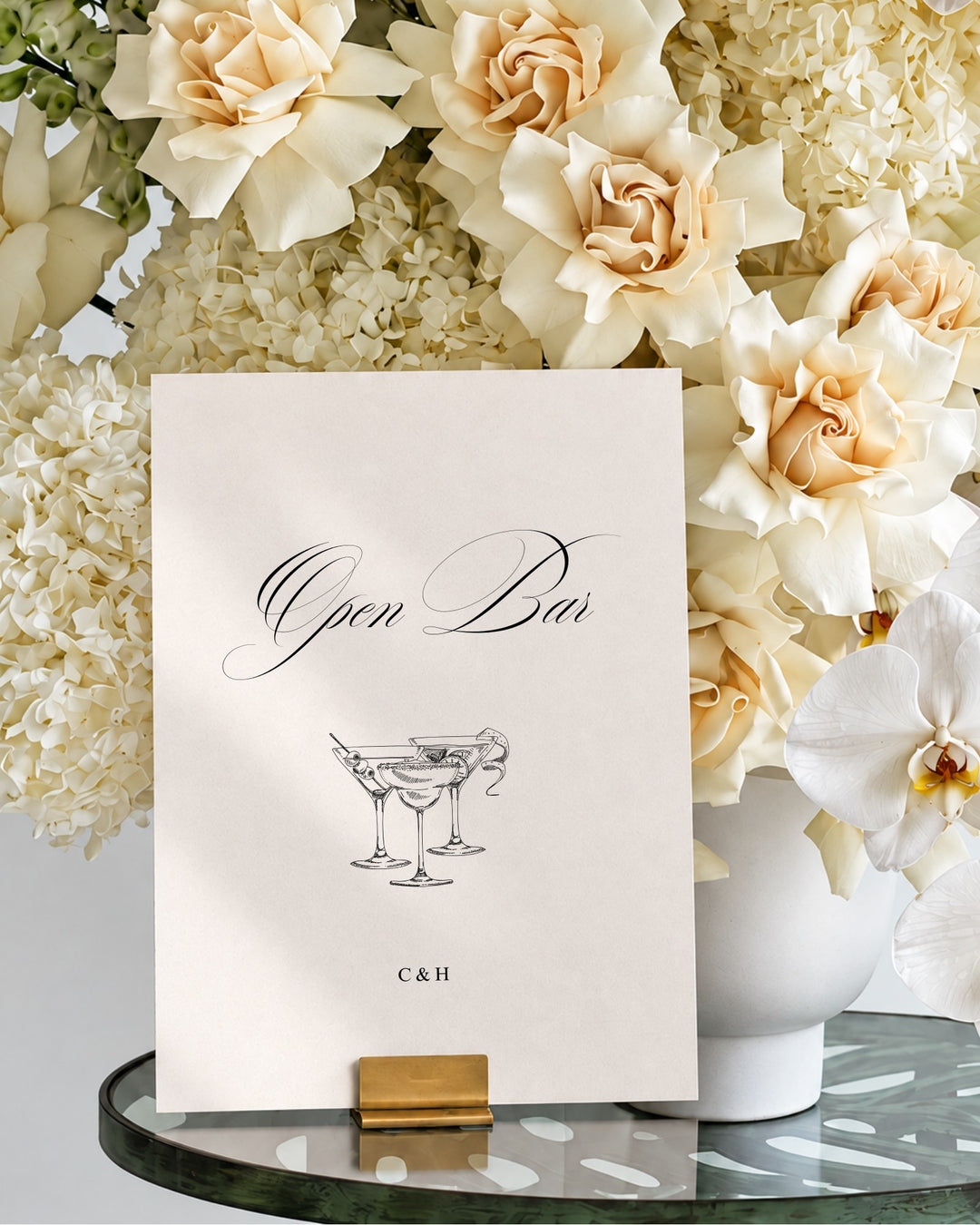 Florence acrylic wedding bar and drinks sign in a gold holder on a glass table in front of ivory roses and hydrangeas