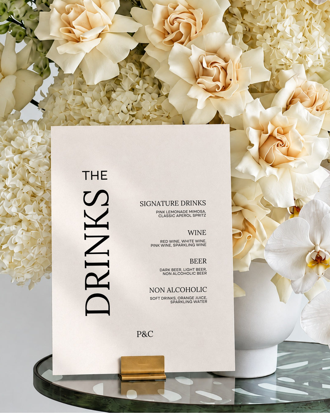 Moda acrylic wedding bar and drinks sign in a gold holder on a glass table in front of ivory roses and hydrangeas