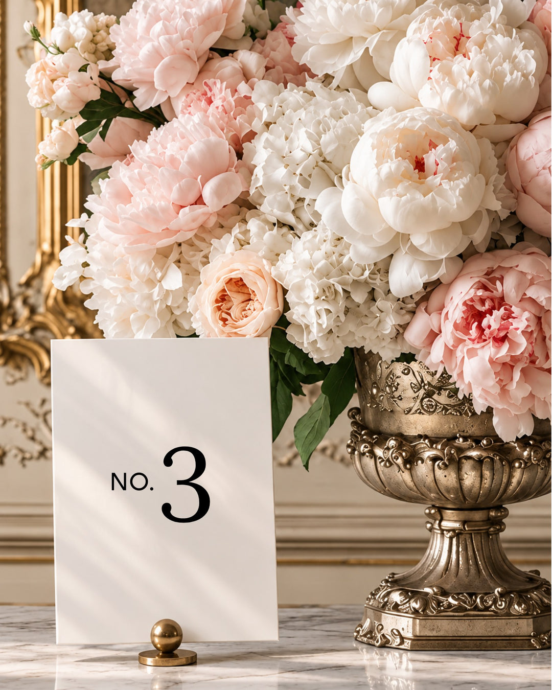 Moda acrylic wedding table number in a gold holder beside blush peonies in a gilded urn