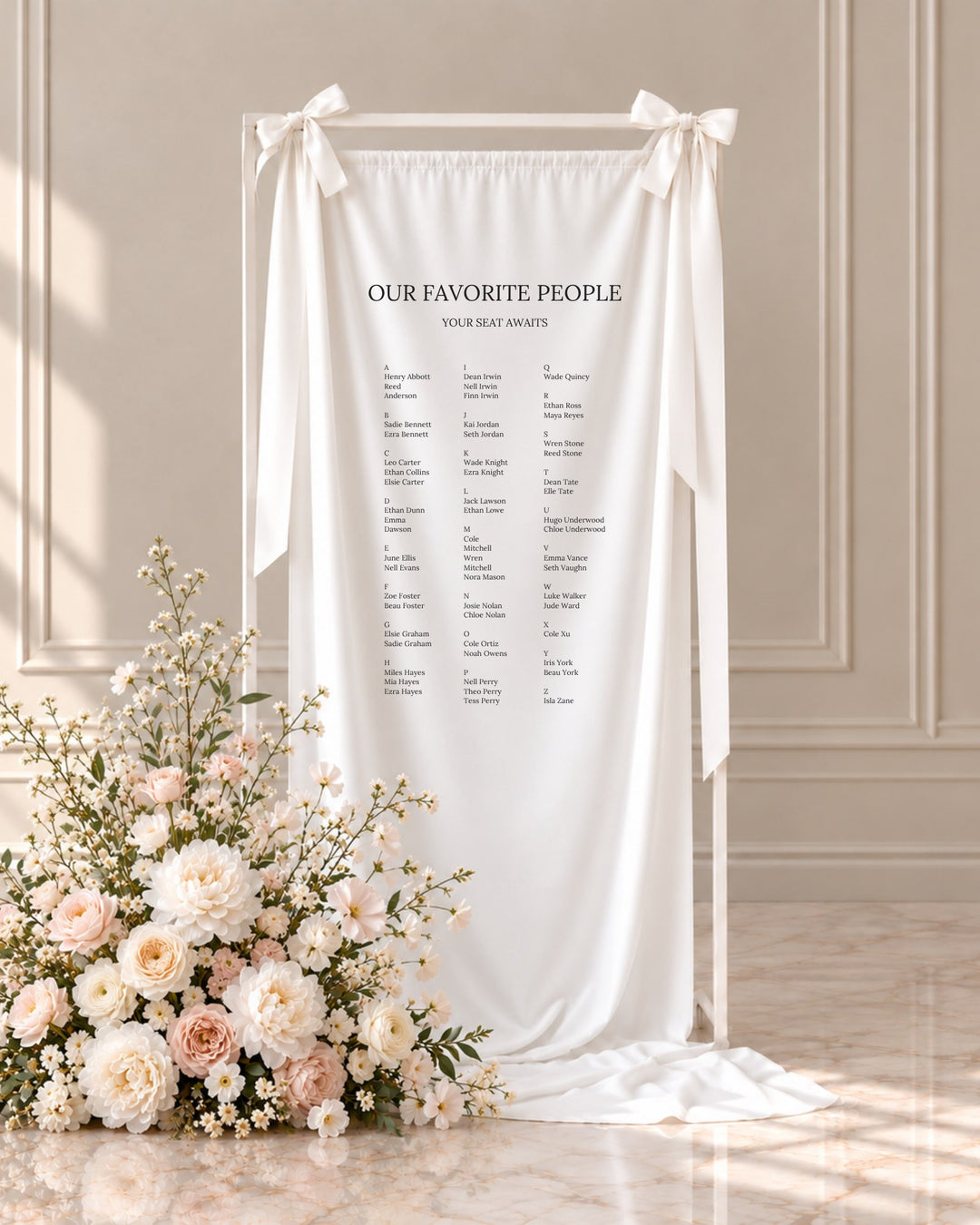 Moda fabric wedding seating chart hanging from a white stand beside blush and ivory florals