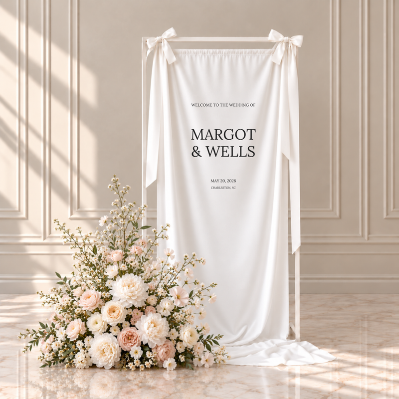 Moda fabric wedding welcome sign: welcome to the wedding of, the couple's names, wedding date and location, hanging from a white frame with ribbon bows beside blush and ivory flowers