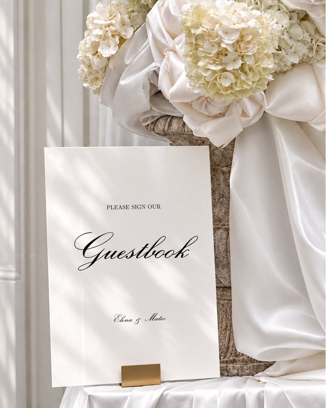 Reina acrylic wedding guestbook sign in a gold holder beside draped ivory silk and hydrangeas