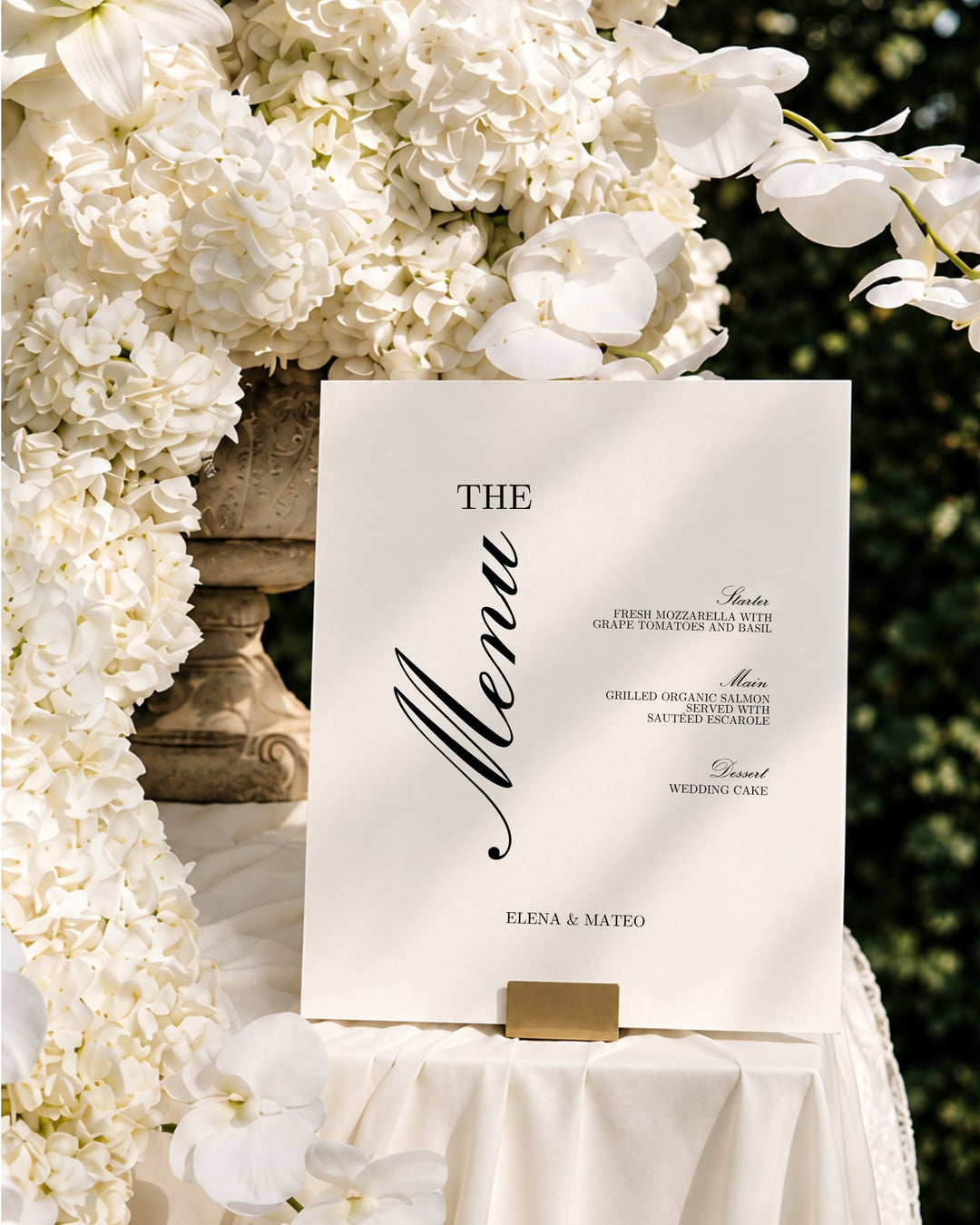 Reina acrylic wedding menu sign in a gold holder among white orchids and hydrangeas