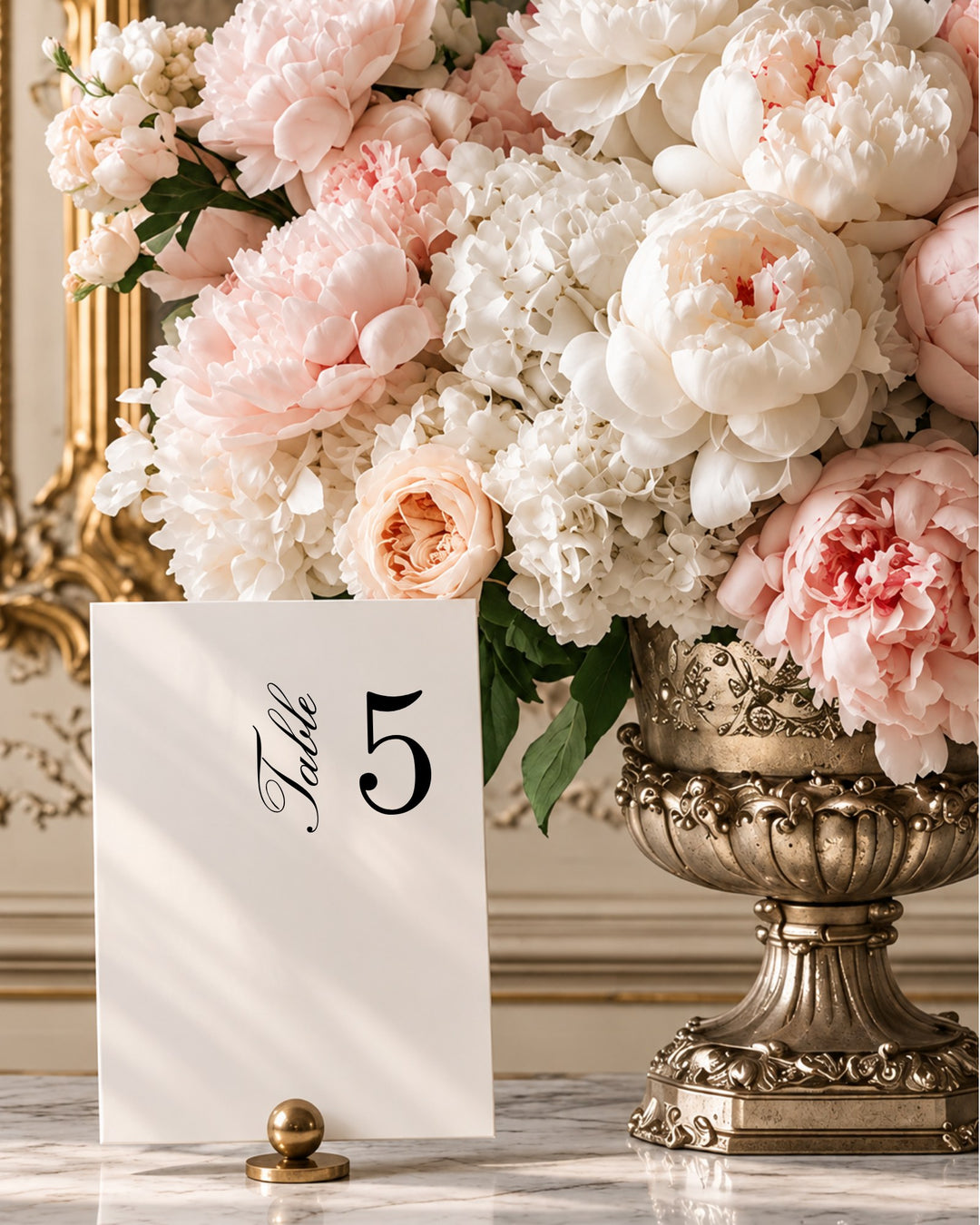 Reina acrylic wedding table number in a gold holder beside blush peonies in a gilded urn