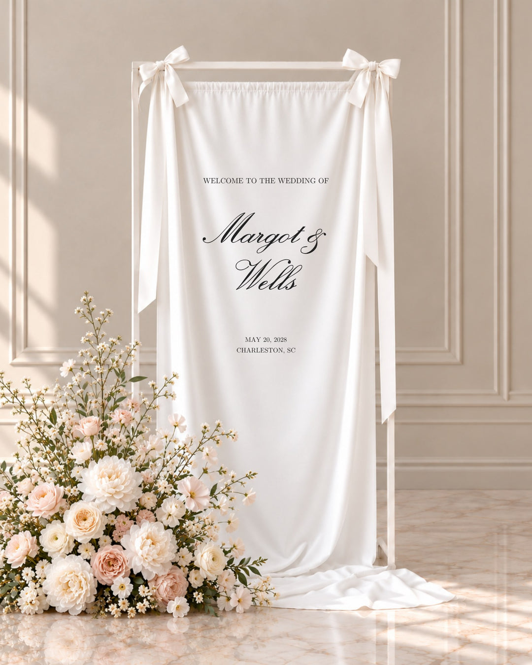 Reina fabric wedding welcome sign hanging from a white stand beside blush and ivory florals