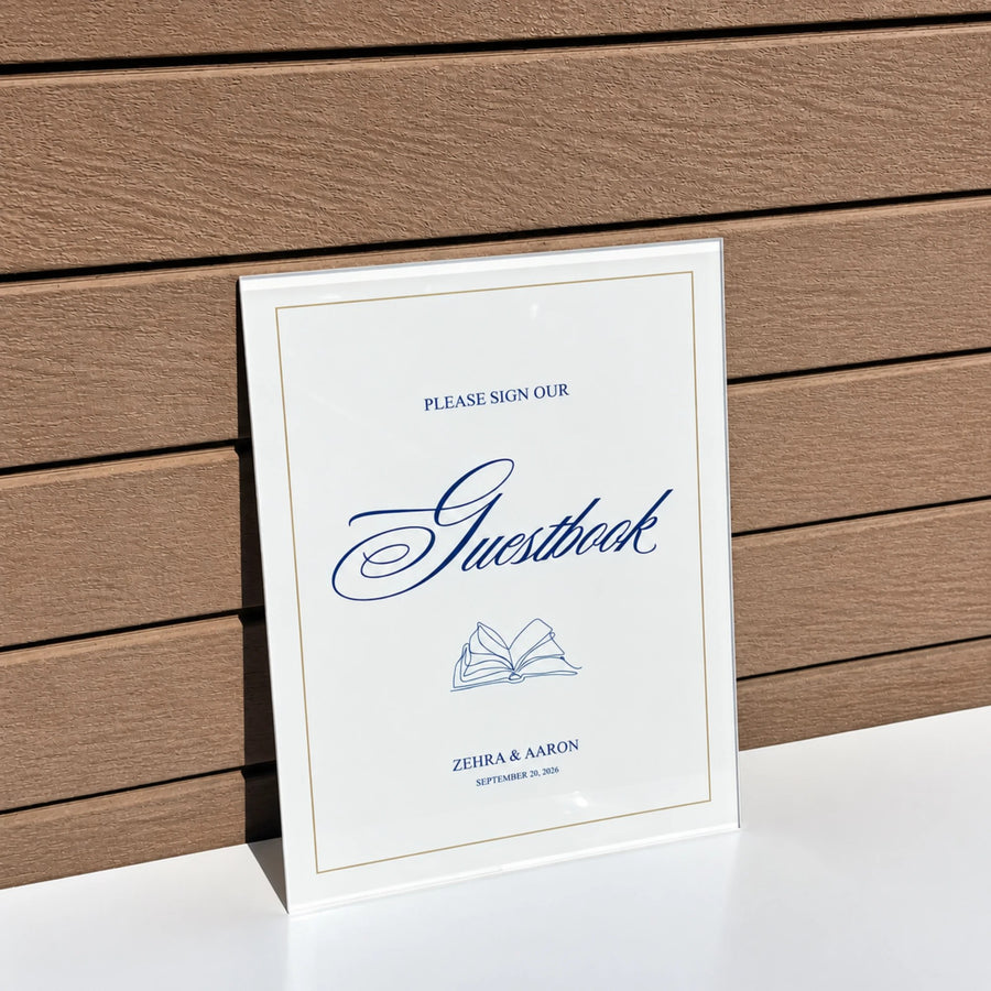 White acrylic guestbook sign in navy script with a gold border